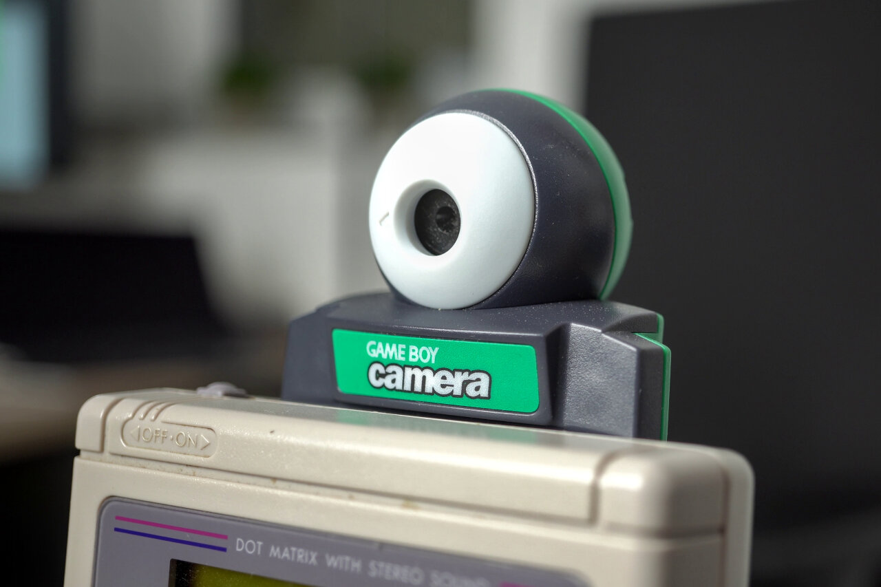 Detail shot of a Game Boy Camera sticking out from a classical Game Boy. The shot shows the camera while only the top edge of the Game Boy is visible.