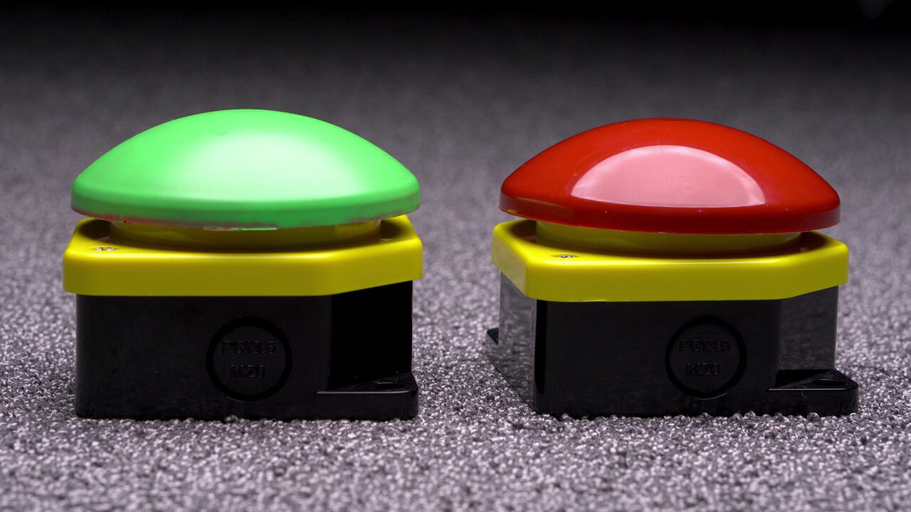 Photo of two large push buttons (the really big emergency stop types). The left one has a green hat, the right one has a red hat.