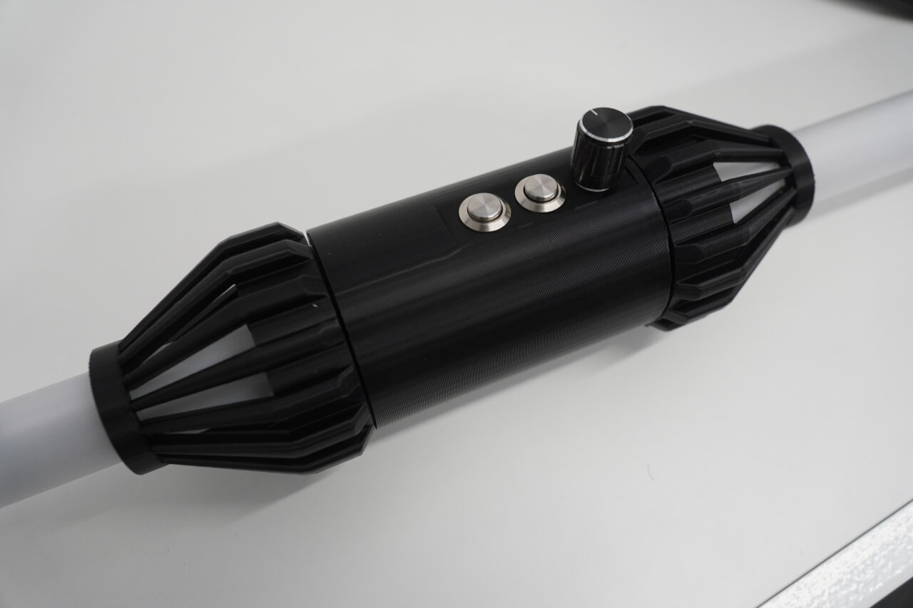 Photo of the assembled grip part of the staff. A black cylinder connected at top and bottom to the white diffusor tubes. On its side it has a knob for the rotary encoder and two metallic push buttons.